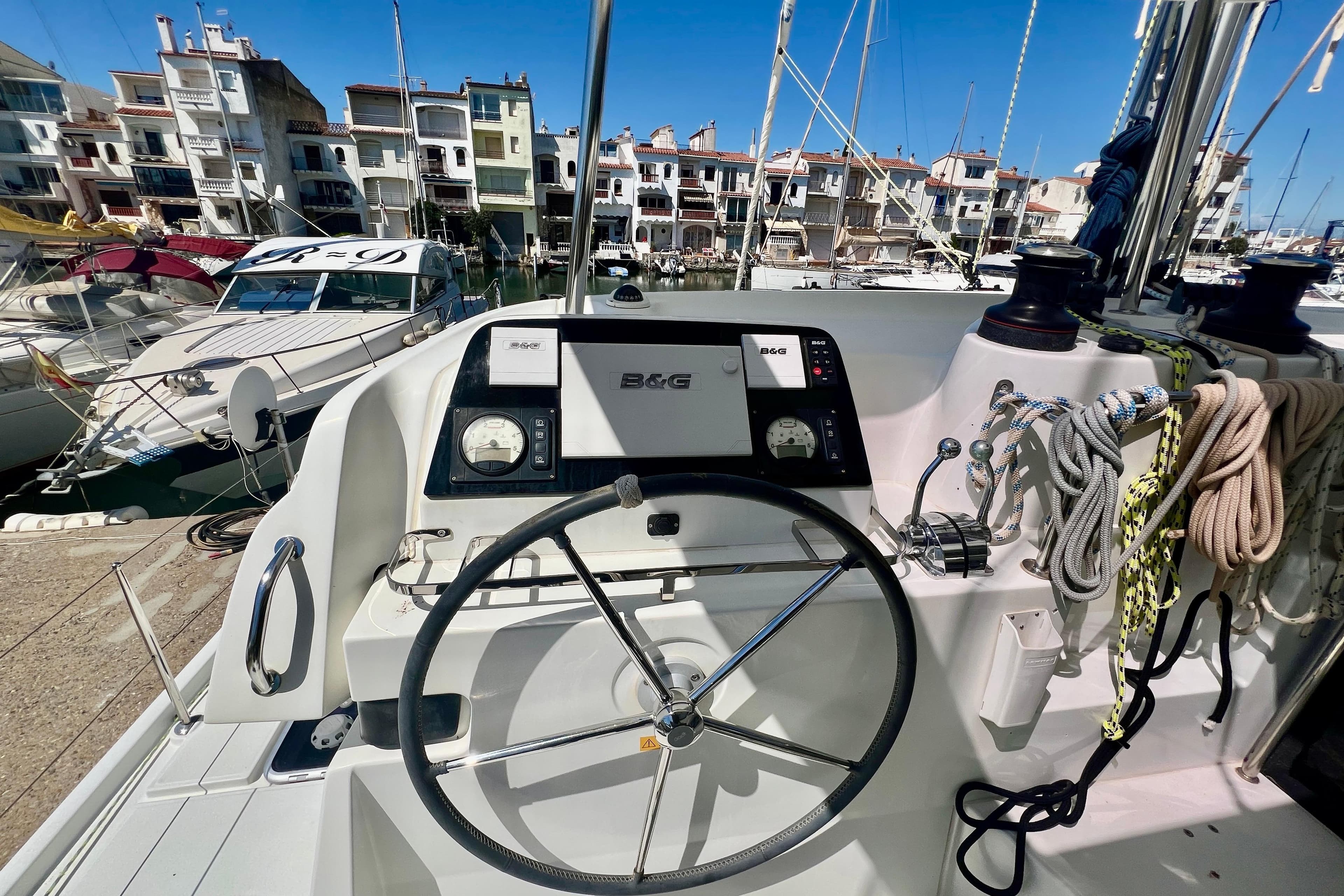 Helm of 2019 Lagoon 42 catamaran in marina, featuring navigation equipment and mooring ropes.