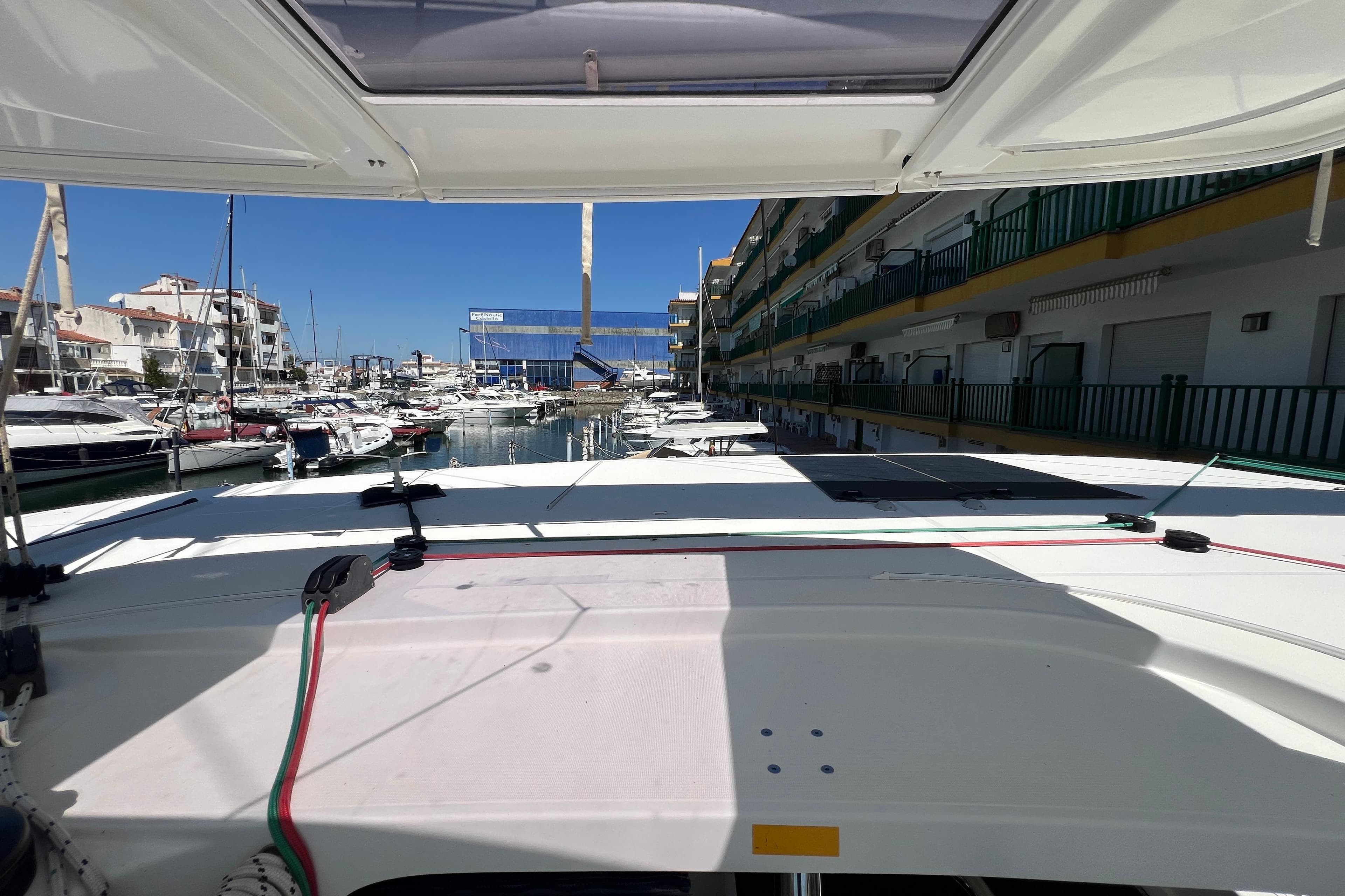 2019 Lagoon 42 catamaran docked in a sunny marina, surrounded by boats and buildings.