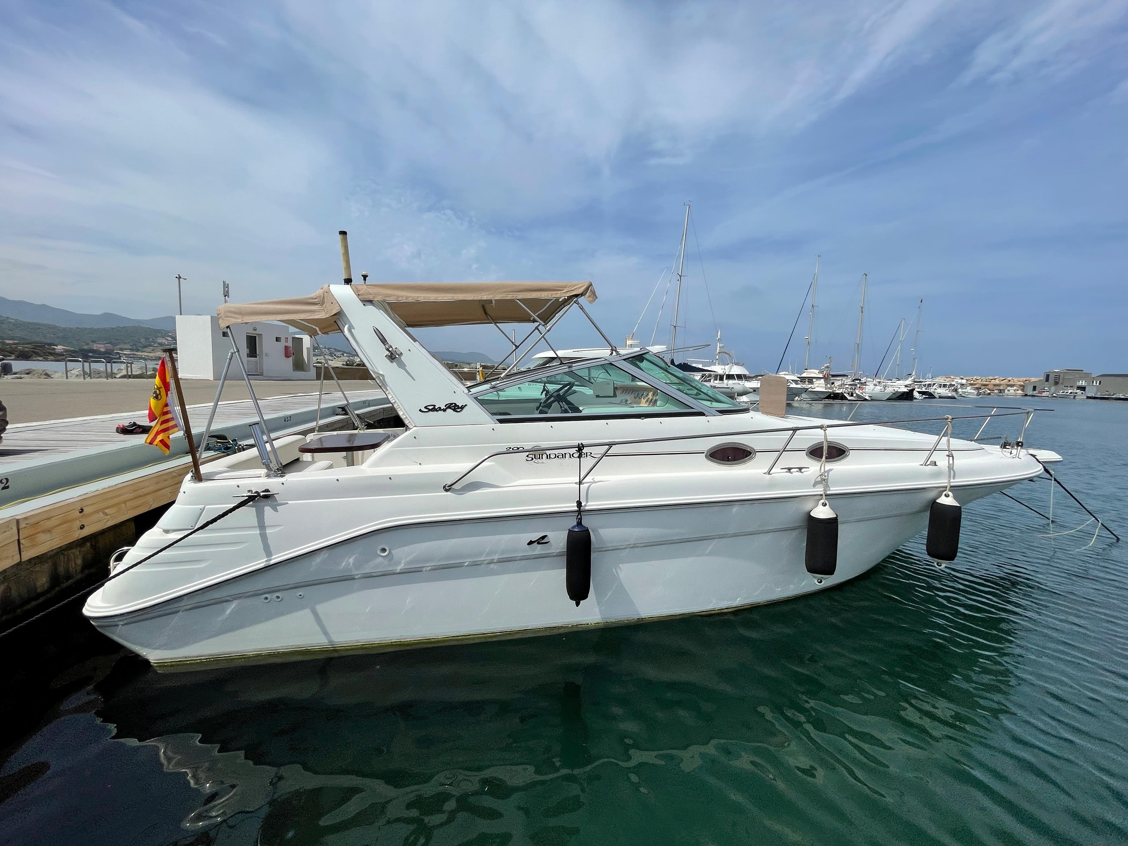 A 1997 Sea Ray 290 Sundancer docked. It features a beige canopy and fenders.