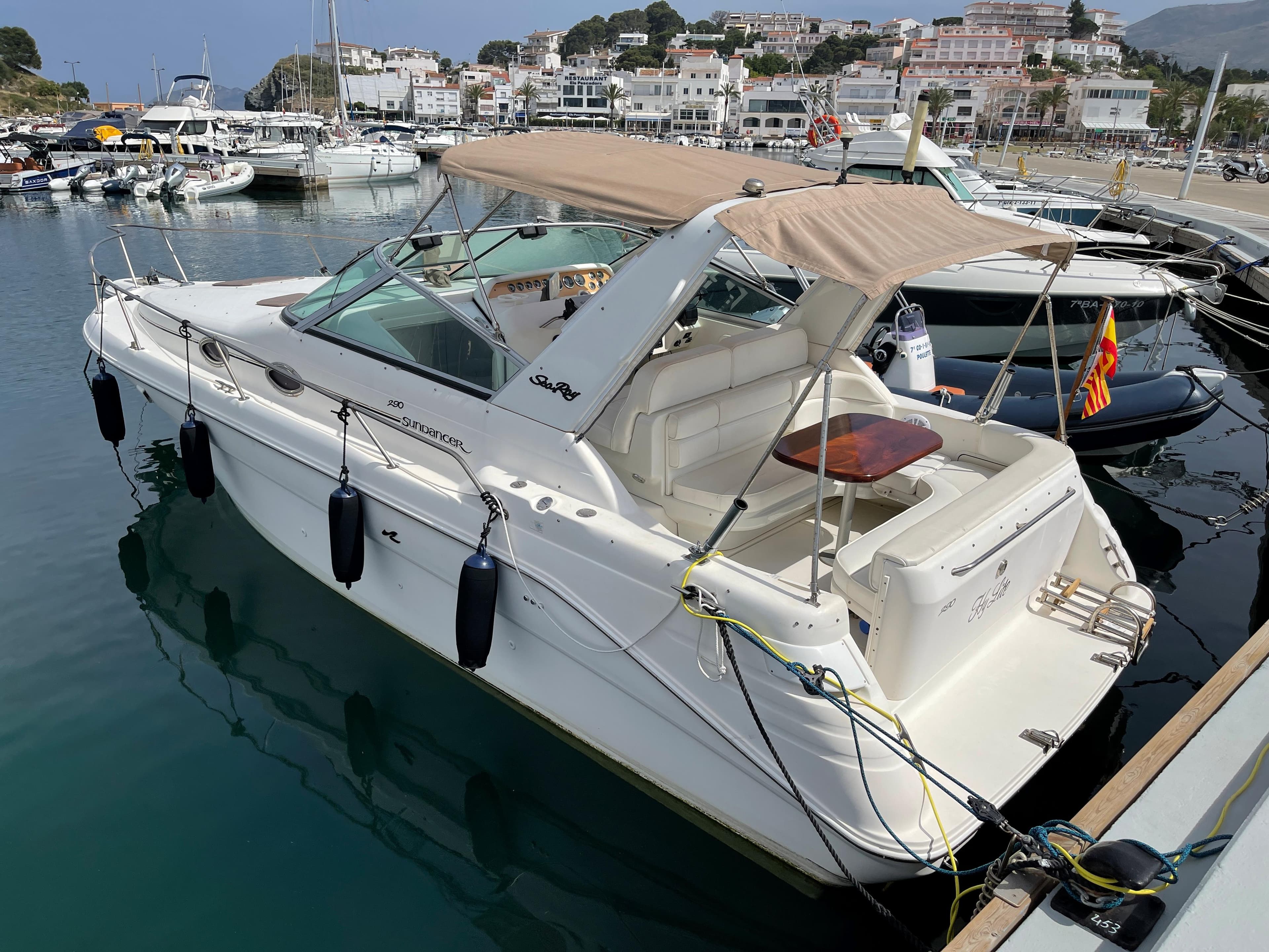 A 1997 Sea Ray 290 Sundancer docked in a marina. It features a beige canopy and fenders.
