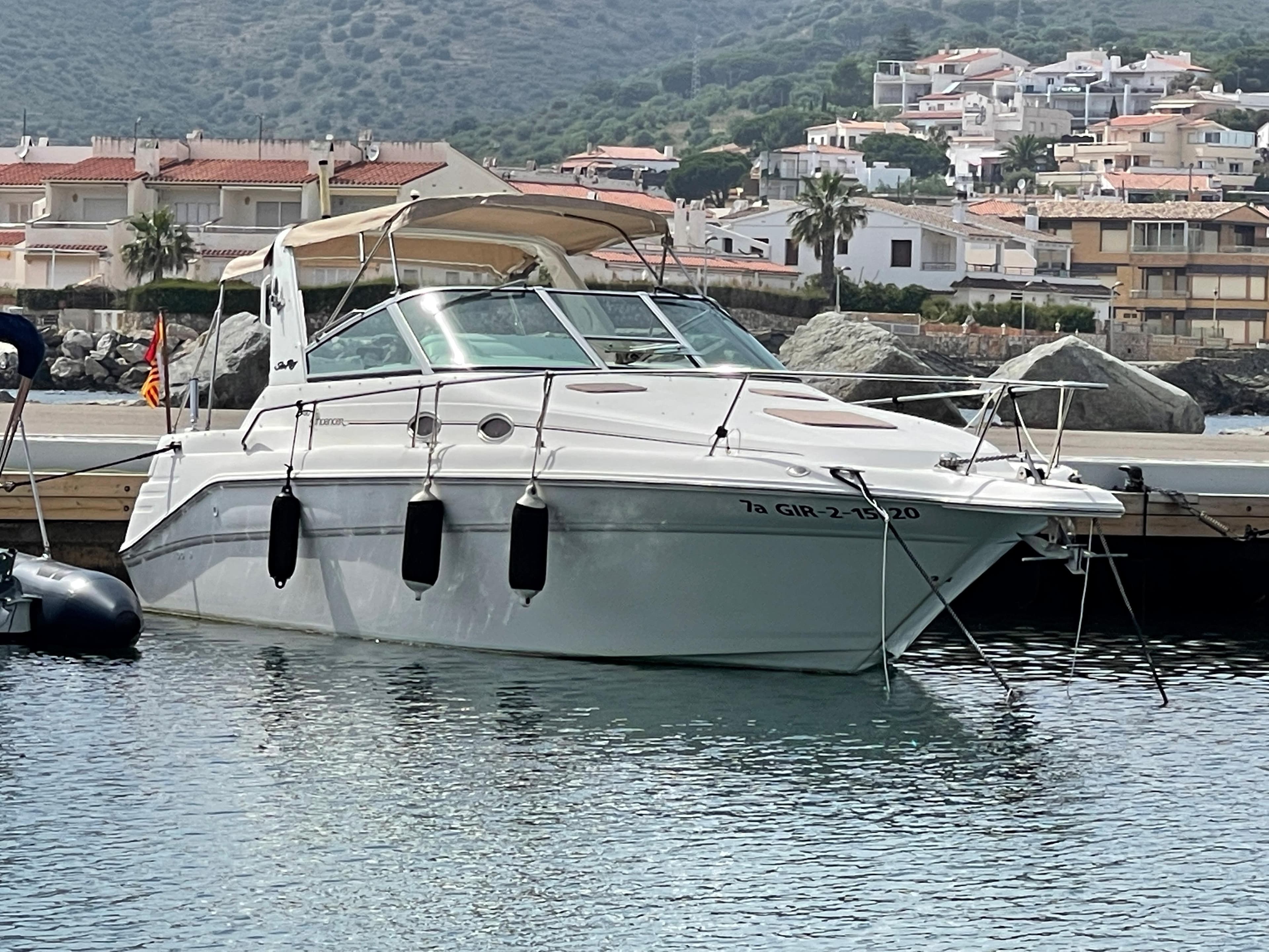 A 1997 Sea Ray 290 Sundancer is anchored in the water, surrounded by buildings and hills.