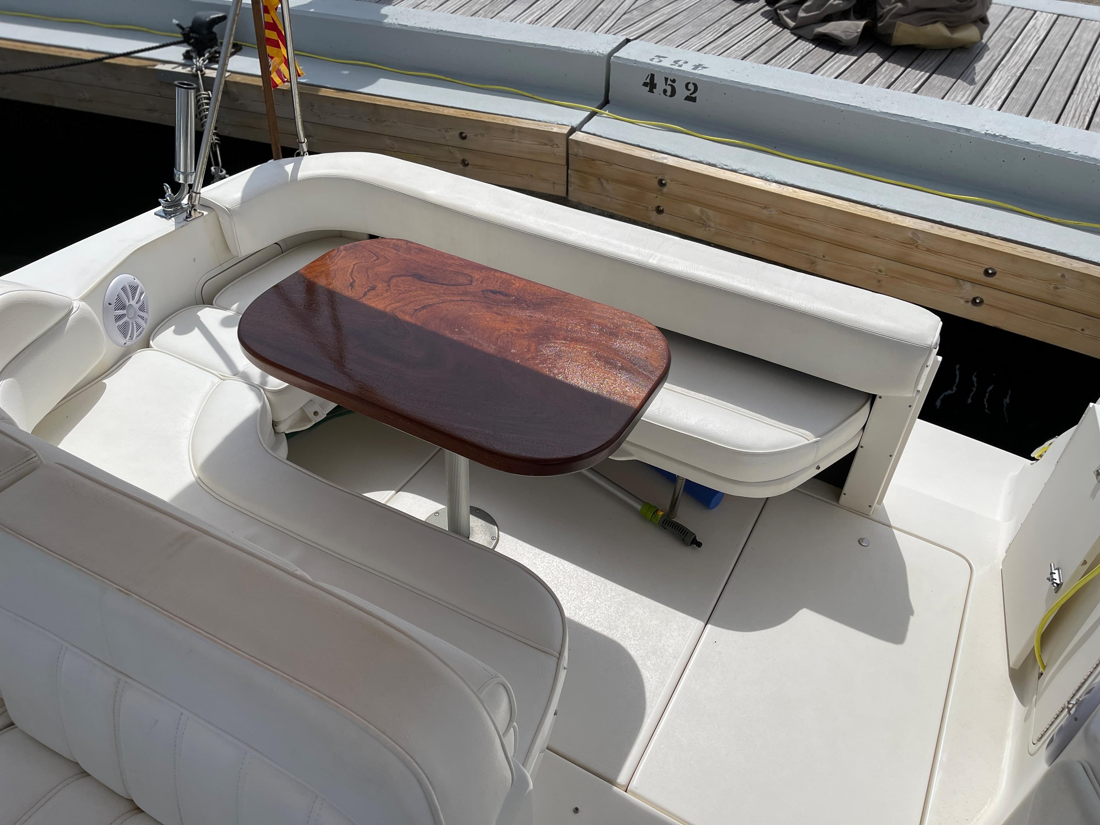 The image shows the seating area of a 1997 Sea Ray 290 Sundancer with a wooden table.