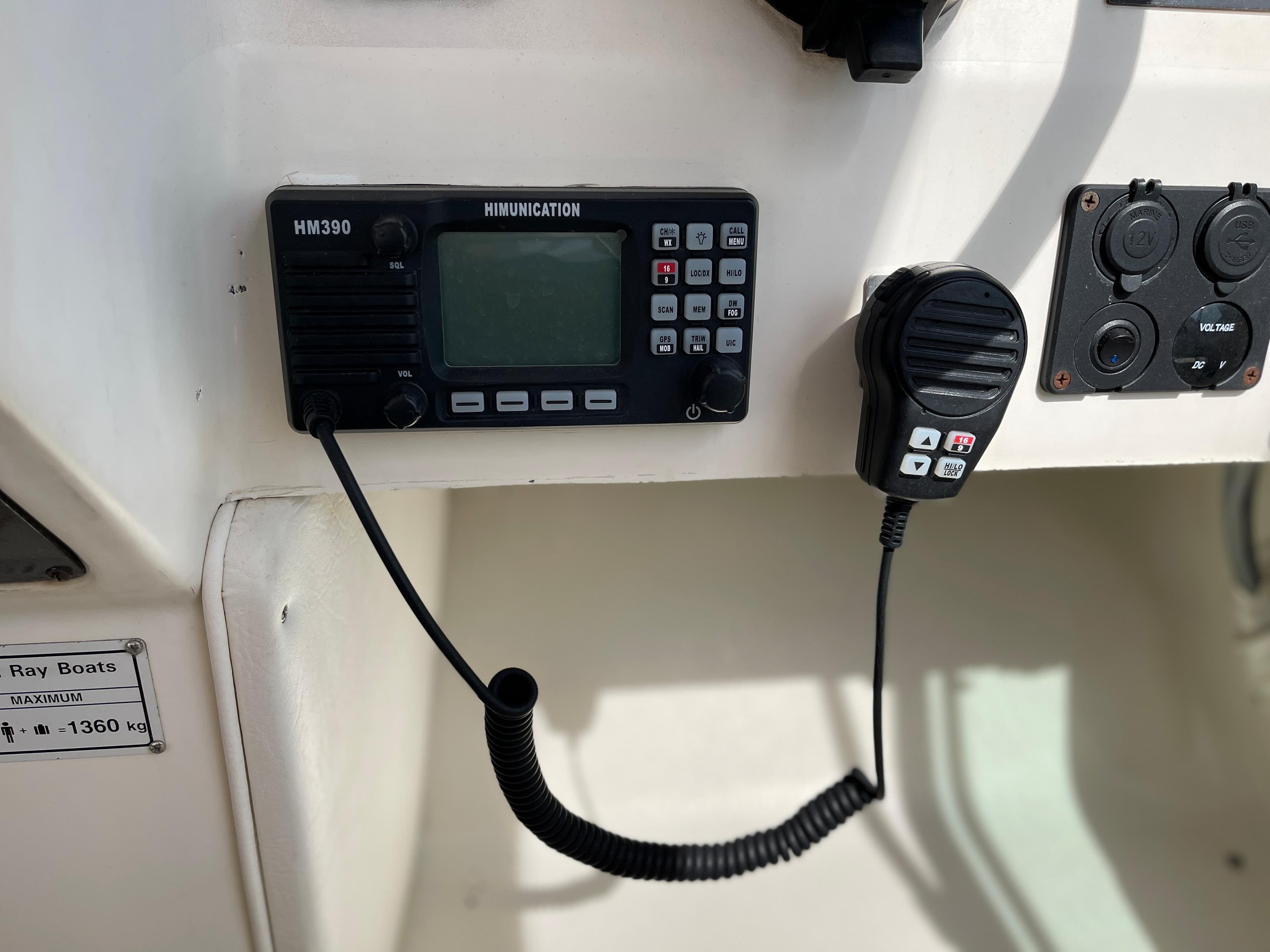 A radio is mounted on a boat's helm console, with a microphone beside it.