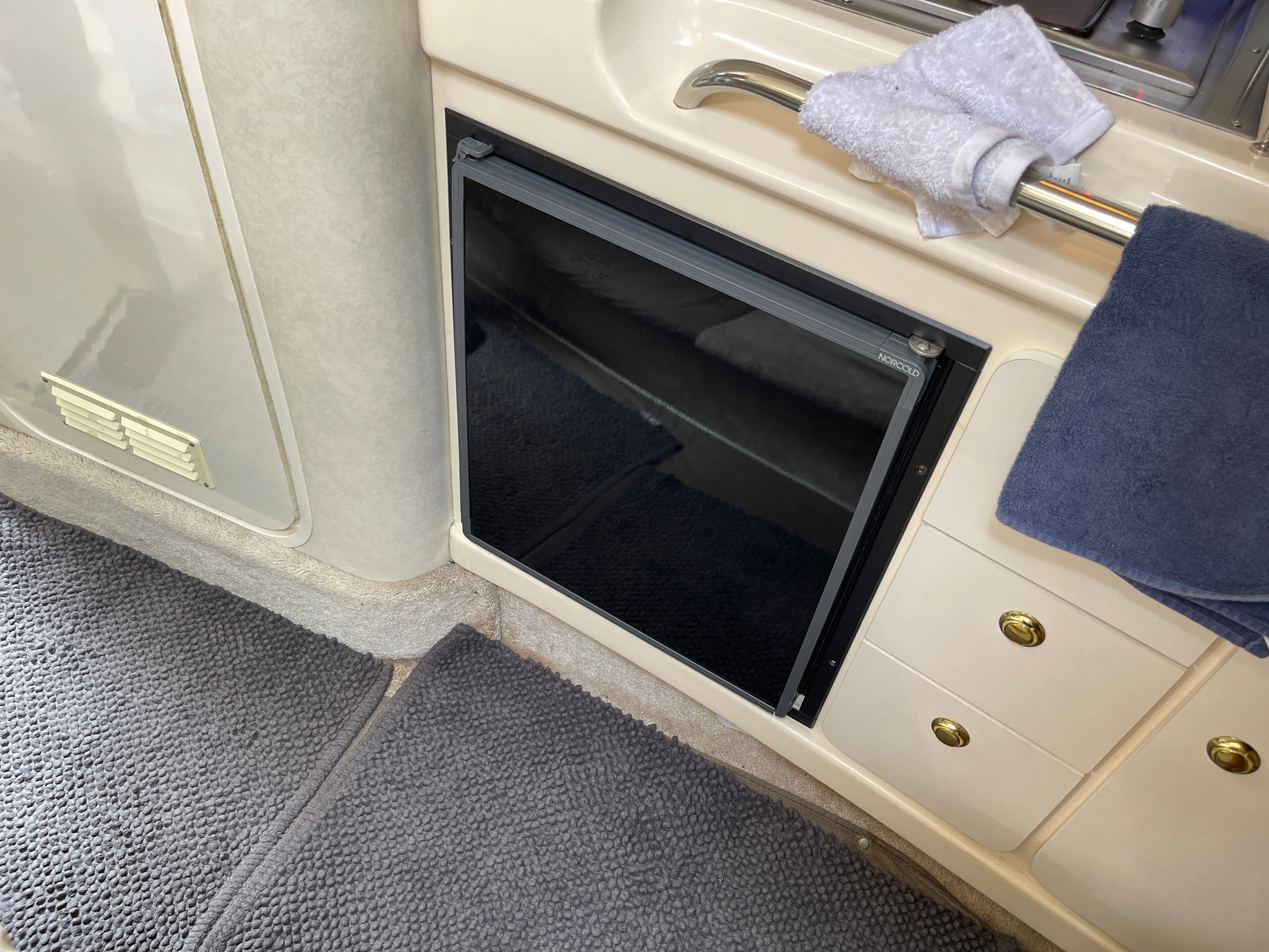 Interior of a 1997 Sea Ray 290 Sundancer featuring a small fridge and towels.