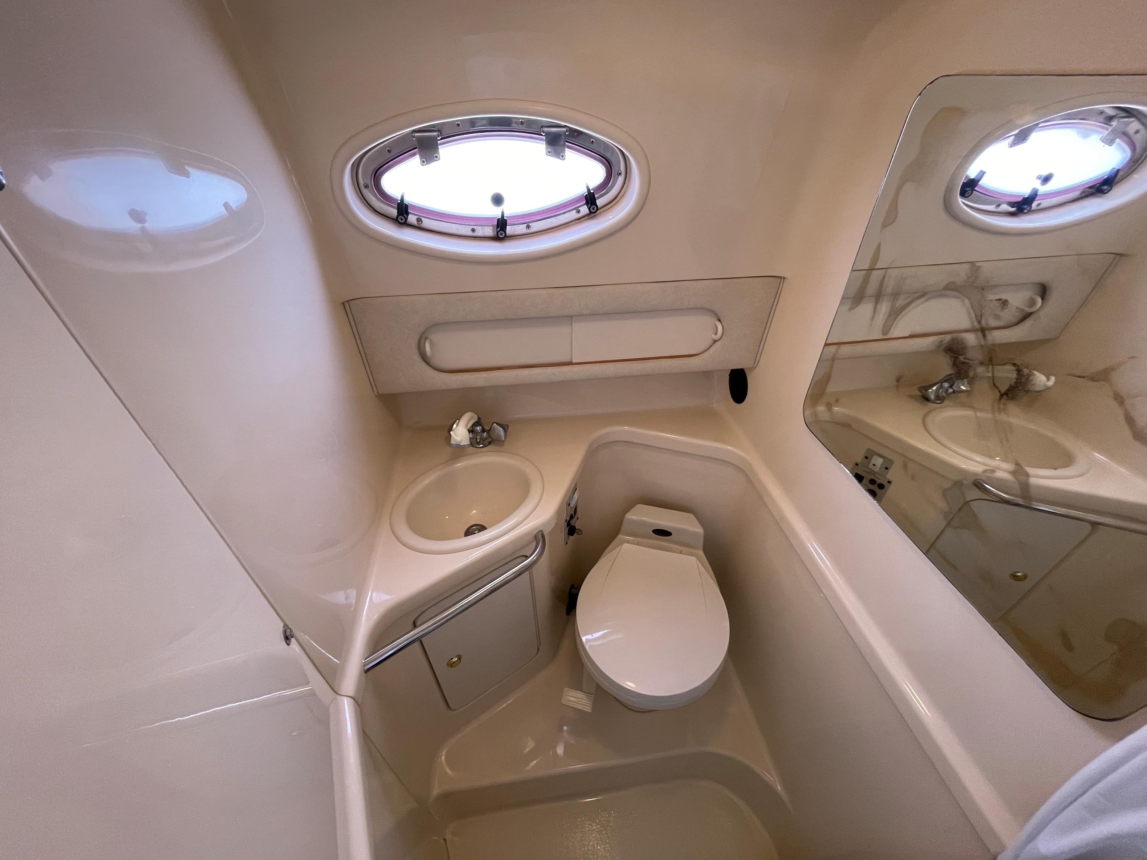 The image shows a boat bathroom with a sink, toilet, and porthole.