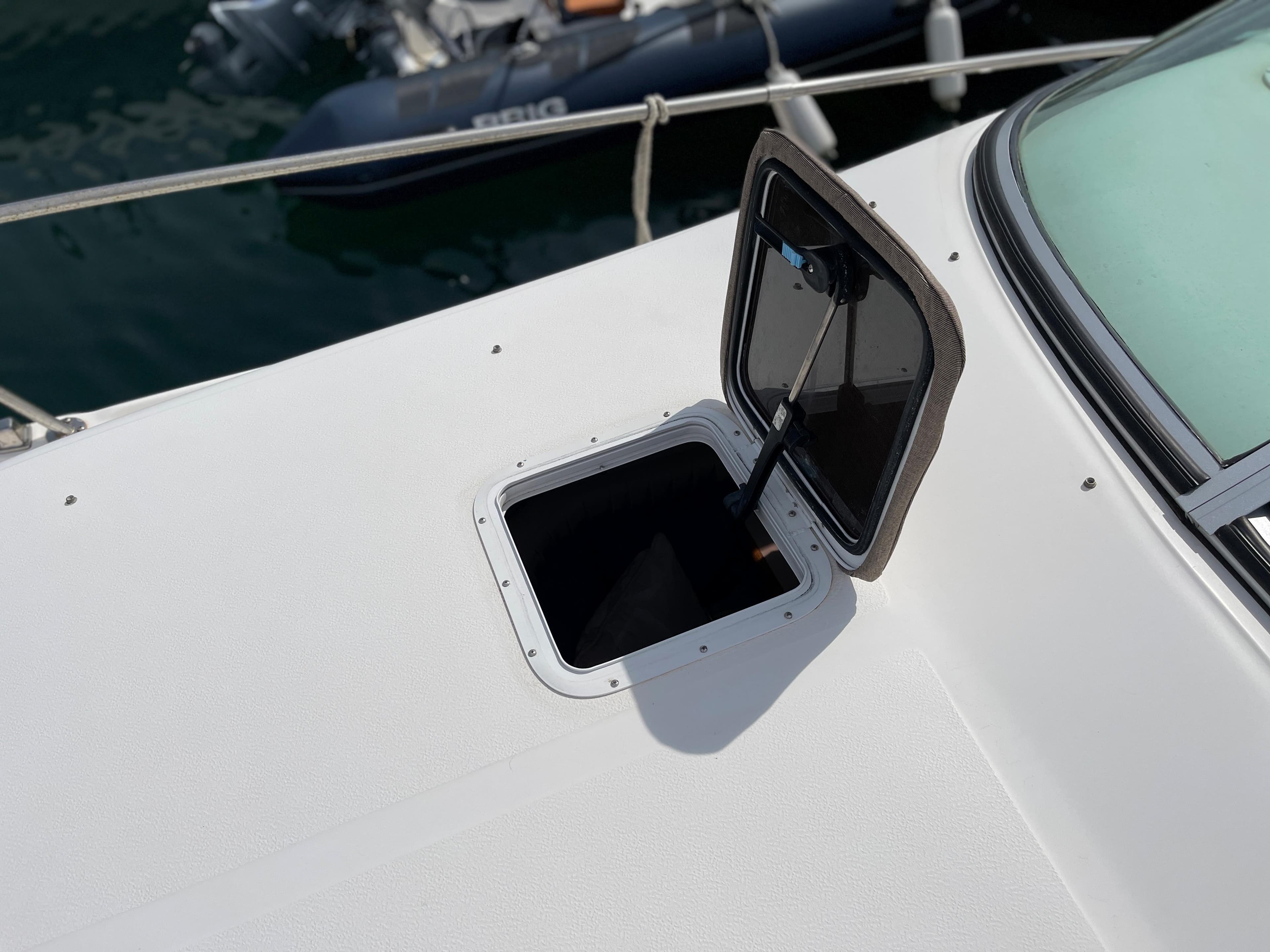 An open deck hatch on a white boat, with an inflatable boat in the background.